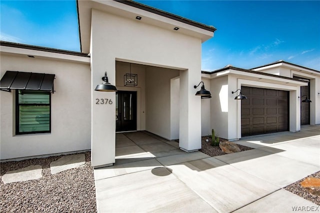 entrance to property with an attached garage, concrete driveway, and stucco siding