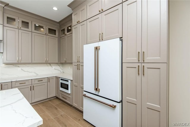 kitchen featuring light stone counters, recessed lighting, backsplash, freestanding refrigerator, and glass insert cabinets