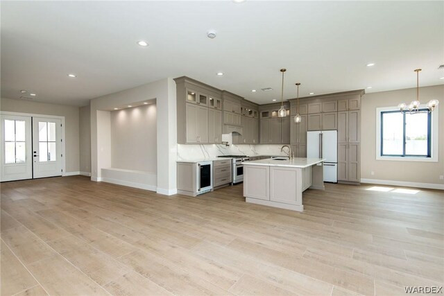 kitchen featuring premium appliances, glass insert cabinets, hanging light fixtures, a kitchen island with sink, and light countertops