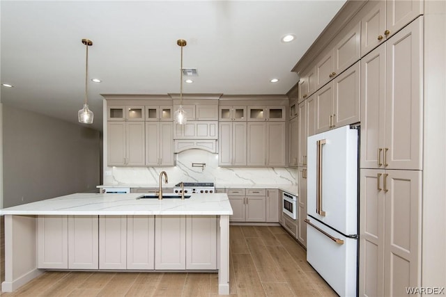 kitchen featuring glass insert cabinets, high end fridge, light stone countertops, pendant lighting, and a sink