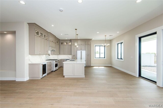 kitchen with an island with sink, glass insert cabinets, light countertops, stainless steel stove, and pendant lighting