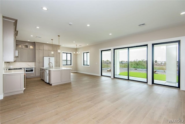 kitchen with glass insert cabinets, open floor plan, hanging light fixtures, a kitchen island with sink, and light countertops