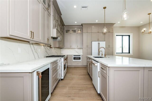 kitchen featuring high end appliances, hanging light fixtures, glass insert cabinets, a sink, and beverage cooler