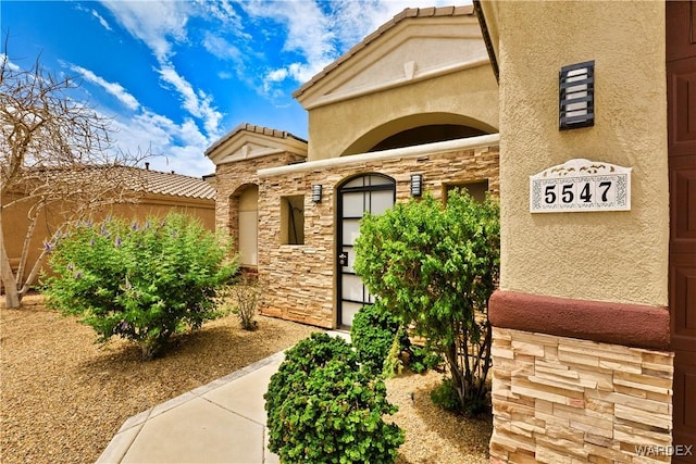 property entrance with stone siding, a tiled roof, and stucco siding