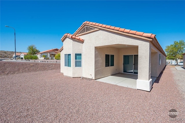 back of house featuring a patio area, a tiled roof, and stucco siding