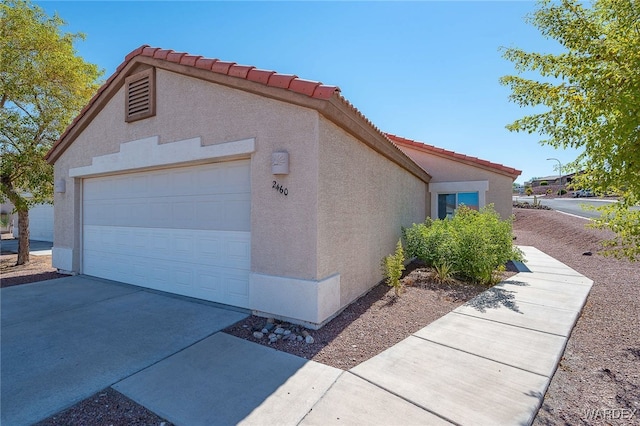 view of side of property featuring a garage, an outdoor structure, driveway, a tiled roof, and stucco siding