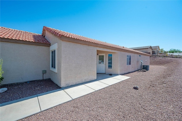 rear view of house with central air condition unit, a tile roof, and stucco siding