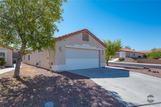 view of front facade featuring an attached garage, a tile roof, concrete driveway, and stucco siding