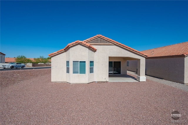 rear view of house with a patio area, a tiled roof, and stucco siding