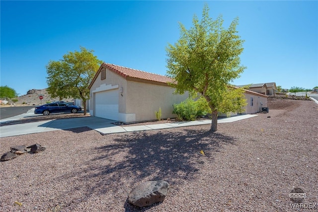 view of property exterior with a garage, driveway, a tiled roof, and stucco siding