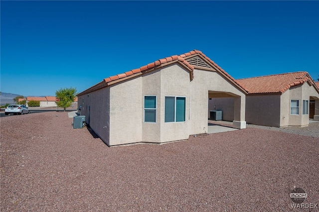 back of house featuring cooling unit, a tile roof, a patio, and stucco siding