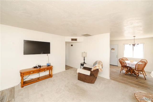 carpeted living room with a textured ceiling, wood finished floors, visible vents, and an inviting chandelier