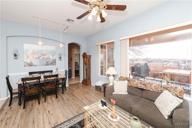 living room featuring arched walkways, ceiling fan, visible vents, light wood-type flooring, and track lighting