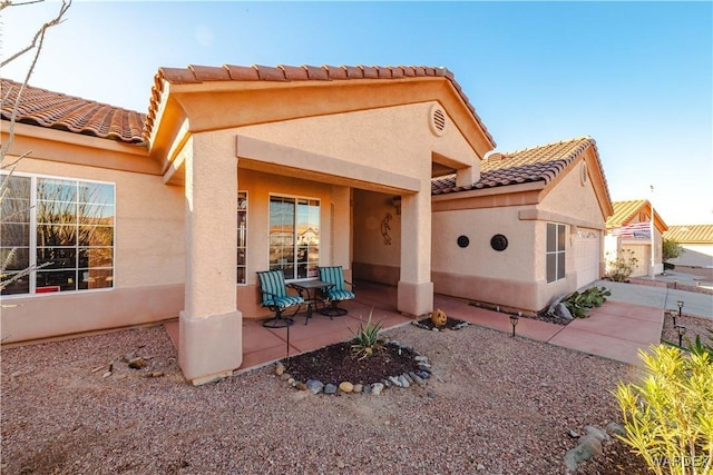 rear view of house with a garage, a tiled roof, a patio area, and stucco siding