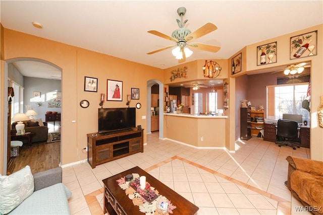 living area with arched walkways, light tile patterned floors, a ceiling fan, and baseboards