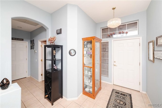 foyer featuring arched walkways, light tile patterned floors, a chandelier, and baseboards