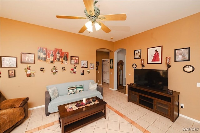 living area with arched walkways, ceiling fan, baseboards, and light tile patterned floors