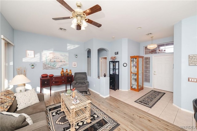 living room with arched walkways, light wood-style flooring, ceiling fan with notable chandelier, visible vents, and baseboards