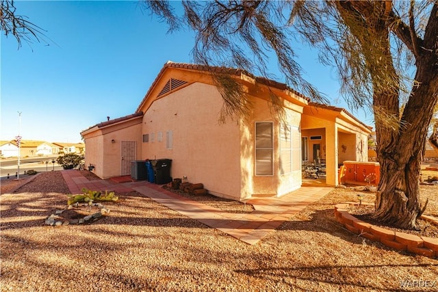 view of side of home with a tile roof, a patio area, a hot tub, and stucco siding