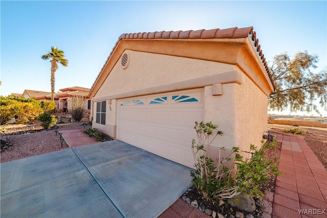 view of property exterior featuring a tile roof, driveway, an attached garage, and stucco siding