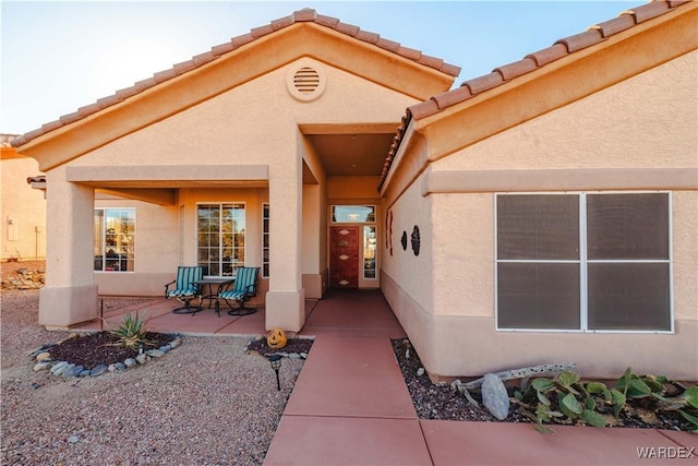 view of exterior entry with a tile roof, a patio, and stucco siding