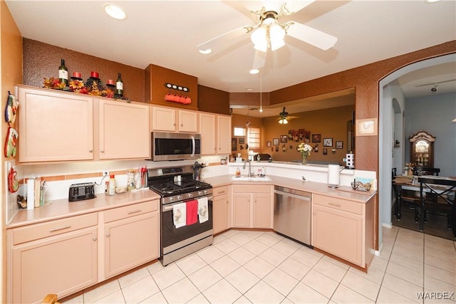 kitchen featuring arched walkways, stainless steel appliances, a peninsula, a sink, and light countertops