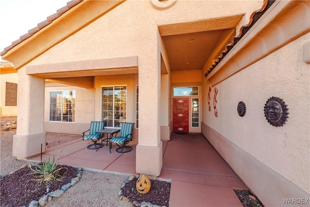 view of exterior entry with a tiled roof, a patio area, and stucco siding