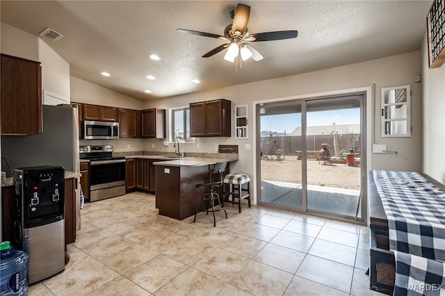 kitchen with visible vents, a kitchen breakfast bar, dark brown cabinetry, a peninsula, and stainless steel appliances