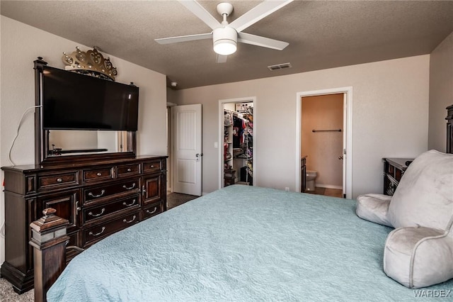 carpeted bedroom with a closet, a spacious closet, ensuite bathroom, visible vents, and ceiling fan