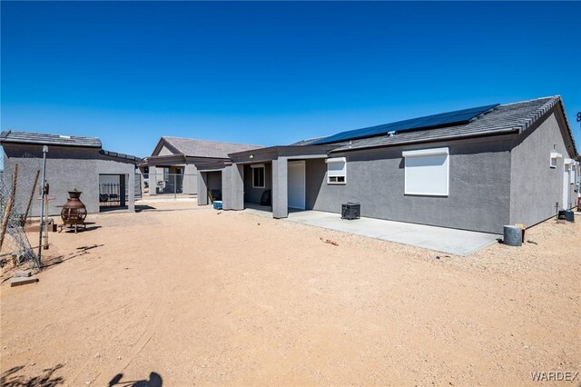 back of property with a patio area, roof mounted solar panels, and stucco siding