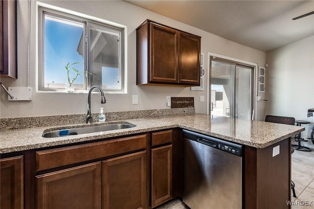 kitchen featuring a sink, a peninsula, dark brown cabinets, stainless steel dishwasher, and light stone counters