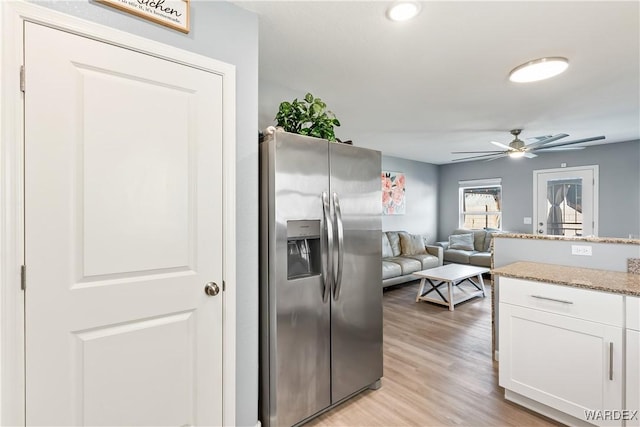 kitchen featuring light wood finished floors, open floor plan, white cabinets, light stone countertops, and stainless steel fridge