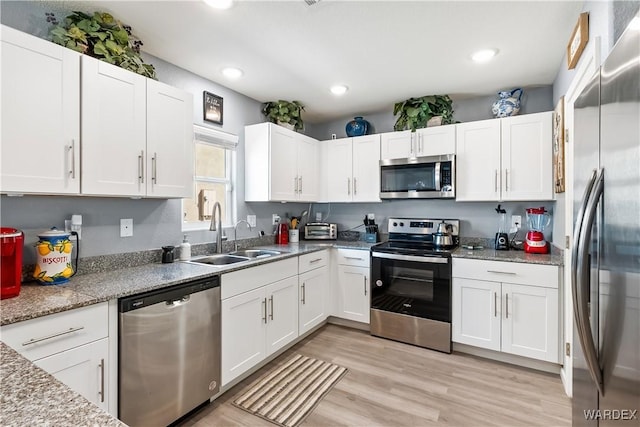 kitchen with appliances with stainless steel finishes, a sink, white cabinetry, and light stone countertops