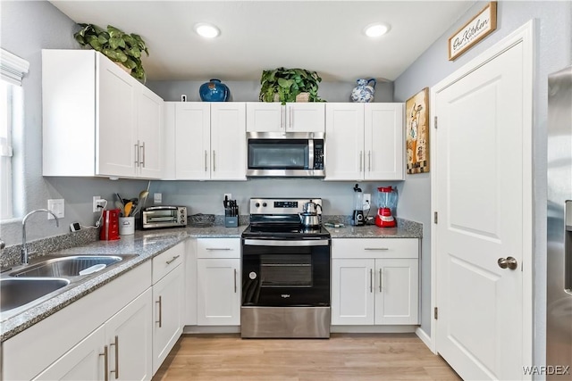 kitchen with appliances with stainless steel finishes, a sink, light wood-style flooring, and white cabinets