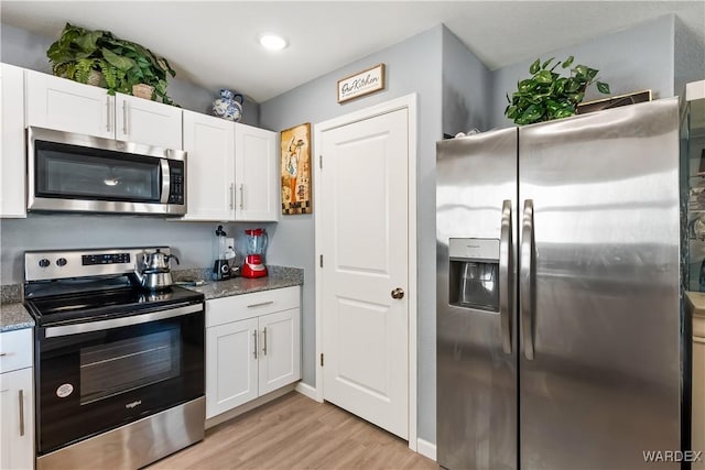 kitchen with light wood-style flooring, appliances with stainless steel finishes, white cabinets, and dark stone counters