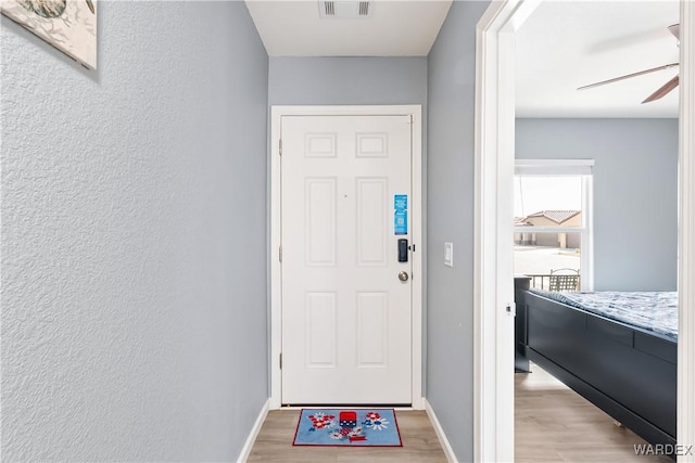 entryway featuring baseboards, visible vents, a ceiling fan, a textured wall, and light wood-type flooring