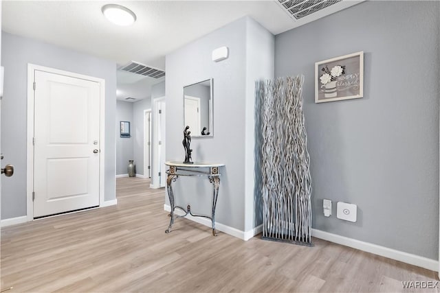 hall with visible vents, light wood-style flooring, and baseboards