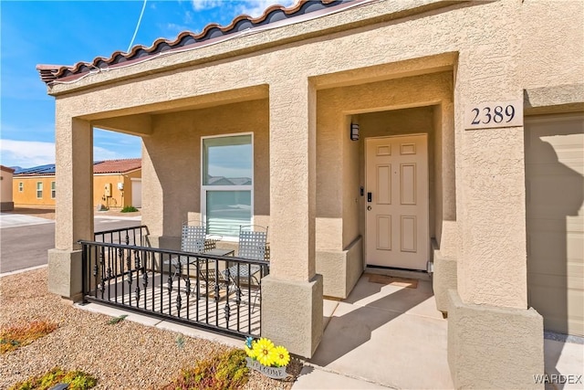 entrance to property with a garage, covered porch, a tiled roof, and stucco siding