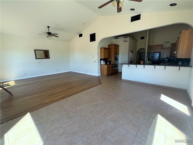 unfurnished living room featuring high vaulted ceiling, light tile patterned floors, arched walkways, and a ceiling fan