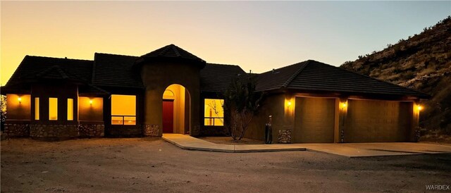 view of front of house with a garage, a tiled roof, stone siding, and stucco siding