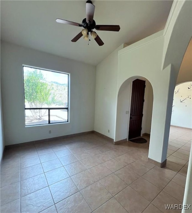 spare room featuring lofted ceiling, arched walkways, light tile patterned flooring, a ceiling fan, and baseboards