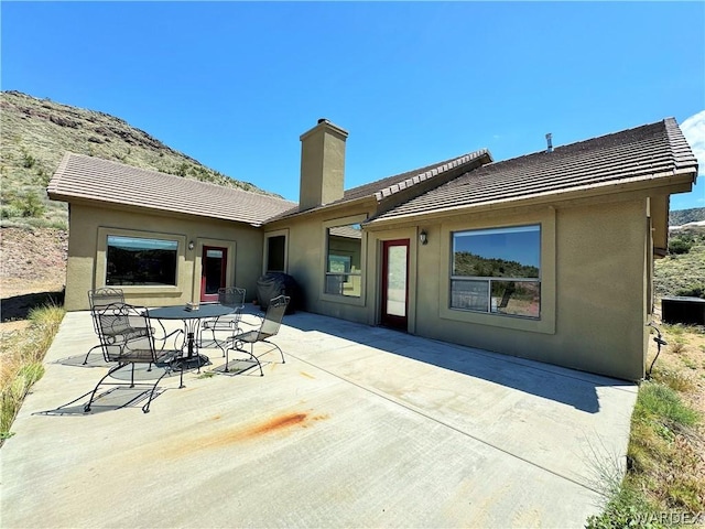 back of house featuring a tiled roof, a patio area, a chimney, and stucco siding