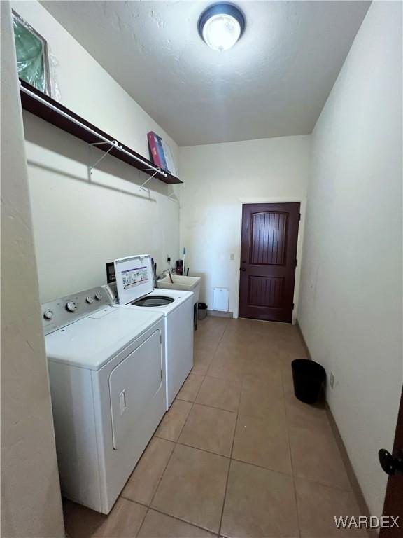 washroom with arched walkways, light tile patterned floors, washing machine and dryer, laundry area, and a sink