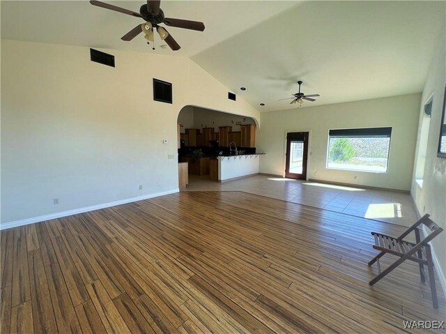 unfurnished living room with arched walkways, visible vents, ceiling fan, wood finished floors, and baseboards