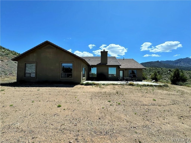 rear view of house with a mountain view, a chimney, and stucco siding