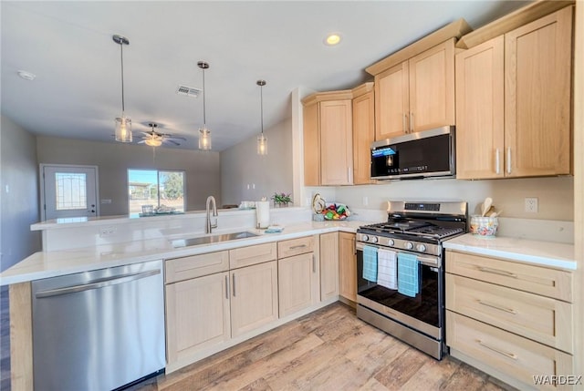 kitchen with a peninsula, appliances with stainless steel finishes, light countertops, and decorative light fixtures