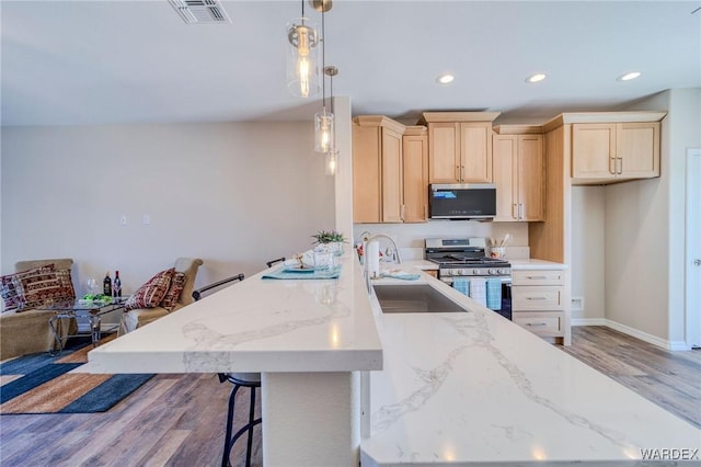 kitchen with stainless steel appliances, visible vents, hanging light fixtures, light brown cabinets, and a sink