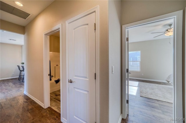 hall with visible vents, baseboards, and dark wood finished floors