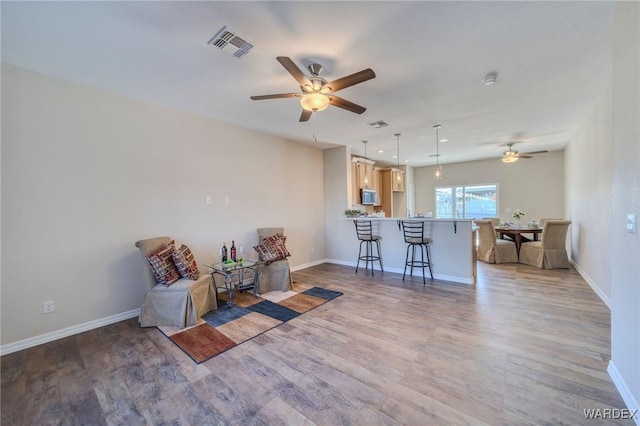 living area featuring light wood-style floors, visible vents, and baseboards