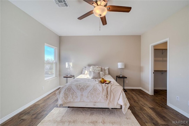 bedroom featuring dark wood-style floors, visible vents, a spacious closet, ceiling fan, and baseboards